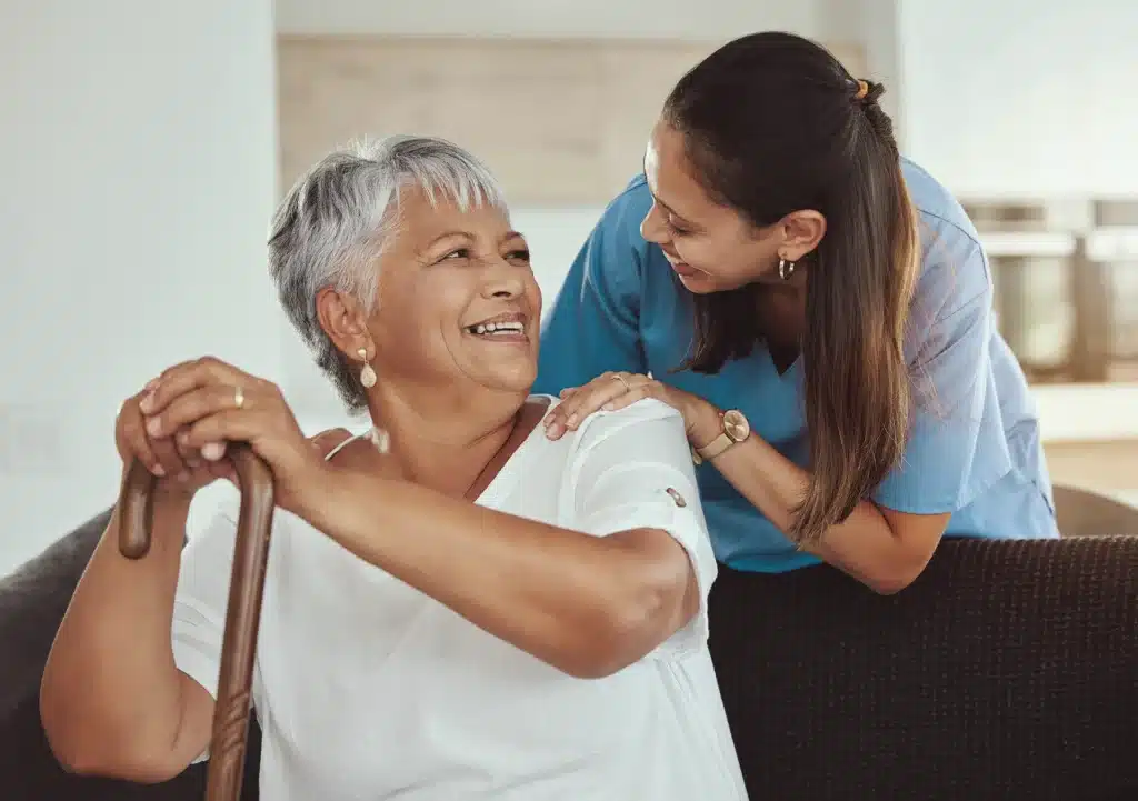 Aide leaning over senior while providing in-home care services and both are smiling at each other