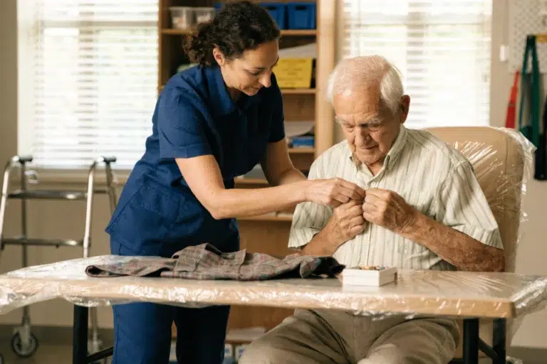 Caregiver assisting an older adult with dressing, an activity of daily living, at home.