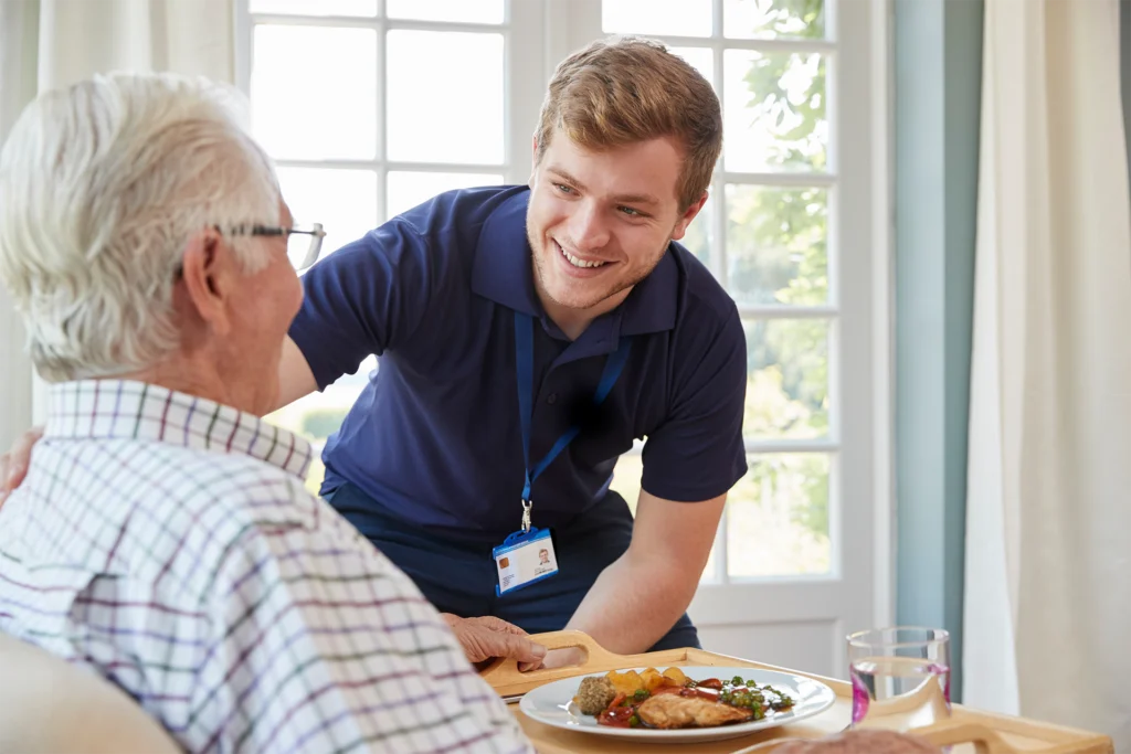 Caregiver assisting an older adult with a meal at home as part of personalized in-home care.